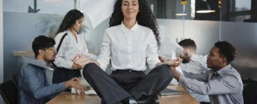 Mulher meditando sobre a mesa em meio ao caos no escritório, simbolizando calma no estresse do trabalho.