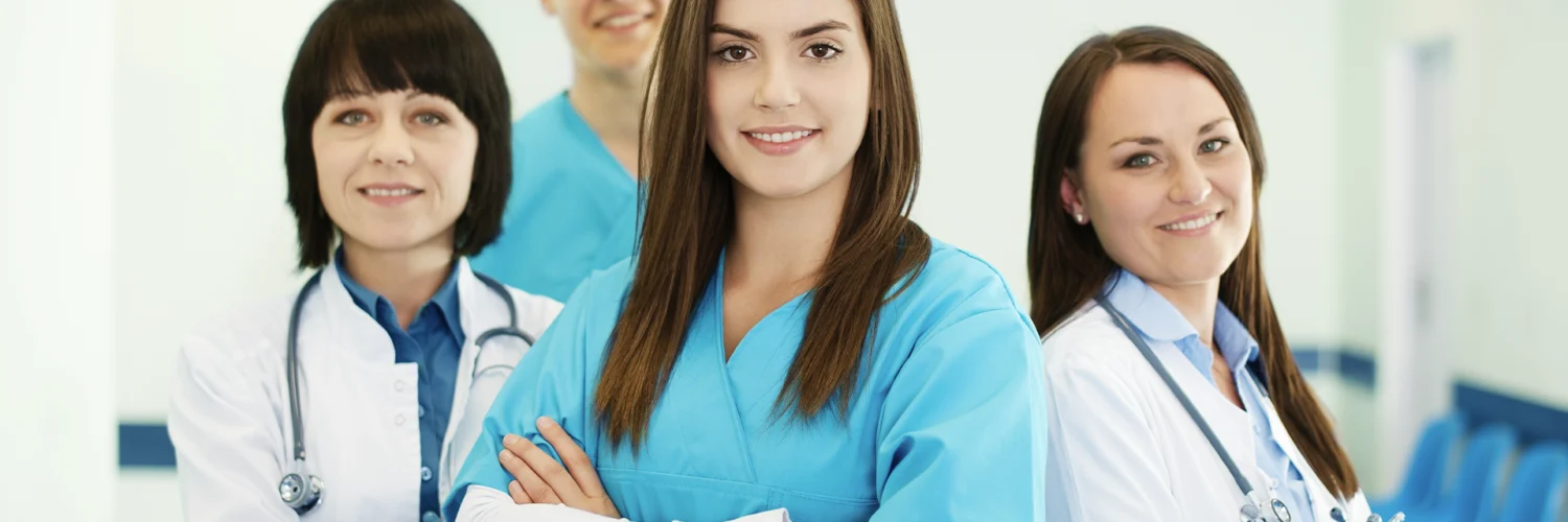 Grupo de profissionais da saúde sorrindo, com roupas médicas, em um ambiente hospitalar iluminado.