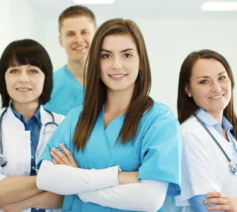 Grupo de profissionais da saúde sorrindo, com roupas médicas, em um ambiente hospitalar iluminado.