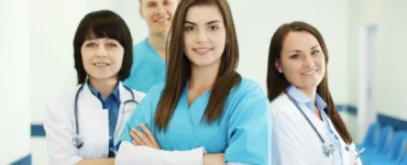 Grupo de profissionais da saúde sorrindo, com roupas médicas, em um ambiente hospitalar iluminado.