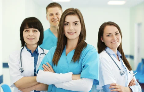 Grupo de profissionais da saúde sorrindo, com roupas médicas, em um ambiente hospitalar iluminado.