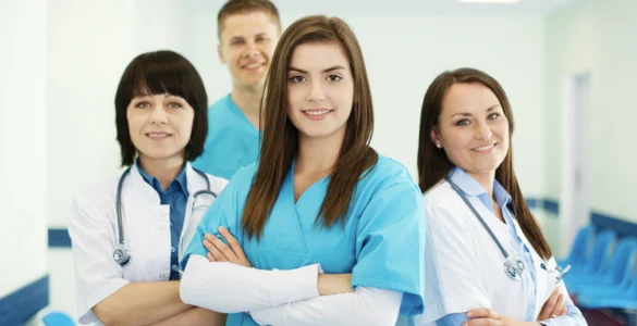 Grupo de profissionais da saúde sorrindo, com roupas médicas, em um ambiente hospitalar iluminado.
