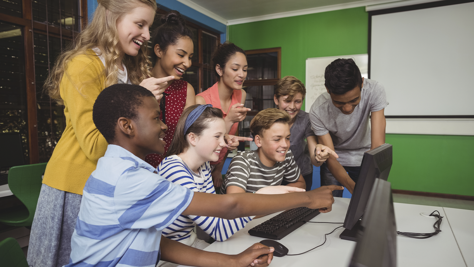 Grupo de alunos se diverte reunido em frente a um computador, aprendendo de forma colaborativa e interativa.