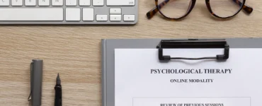 Mesa com teclado, óculos, caneta e ficha de terapia psicológica online com anotações de sessões anteriores.