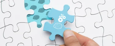 Mão inserindo uma peça de quebra-cabeça azul com ícones de cérebro e engrenagens em um quebra-cabeça branco.