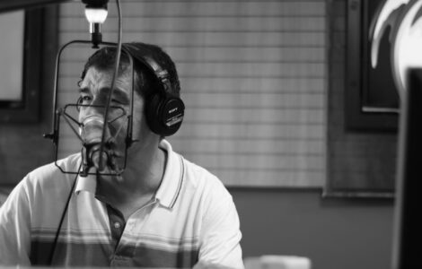 Homem com fones de ouvido fala ao microfone em estúdio de rádio, em imagem em preto e branco.
