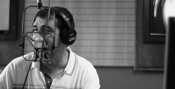 Homem com fones de ouvido fala ao microfone em estúdio de rádio, em imagem em preto e branco.