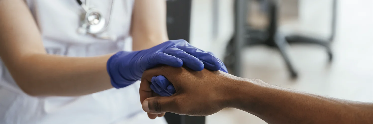 Profissional de saúde segurando a mão de um paciente, demonstrando cuidado e empatia no atendimento.