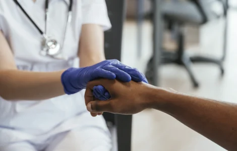 Profissional de saúde segurando a mão de um paciente, demonstrando cuidado e empatia no atendimento.