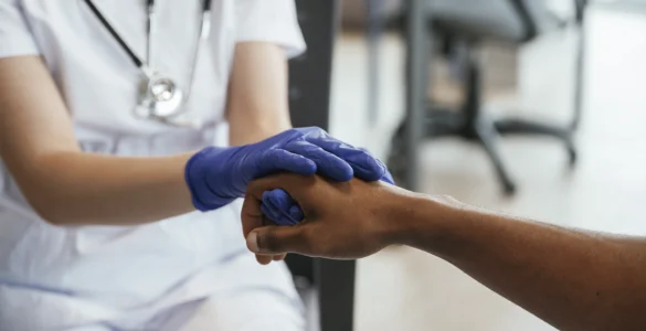 Profissional de saúde segurando a mão de um paciente, demonstrando cuidado e empatia no atendimento.