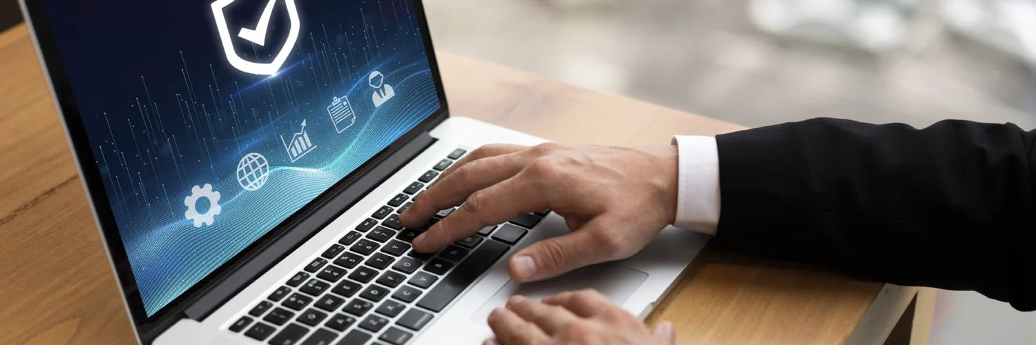 Homem de terno digitando em um laptop com ícones de segurança cibernética e um escudo com um "tick" na tela.