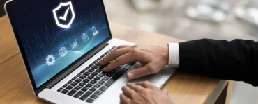 Homem de terno digitando em um laptop com ícones de segurança cibernética e um escudo com um "tick" na tela.