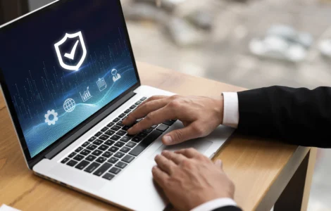 Homem de terno digitando em um laptop com ícones de segurança cibernética e um escudo com um "tick" na tela.