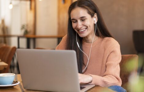 Mulher sorridente com fones de ouvido participa de videochamada em notebook em um café aconchegante.