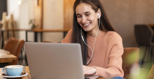 Mulher sorridente com fones de ouvido participa de videochamada em notebook em um café aconchegante.