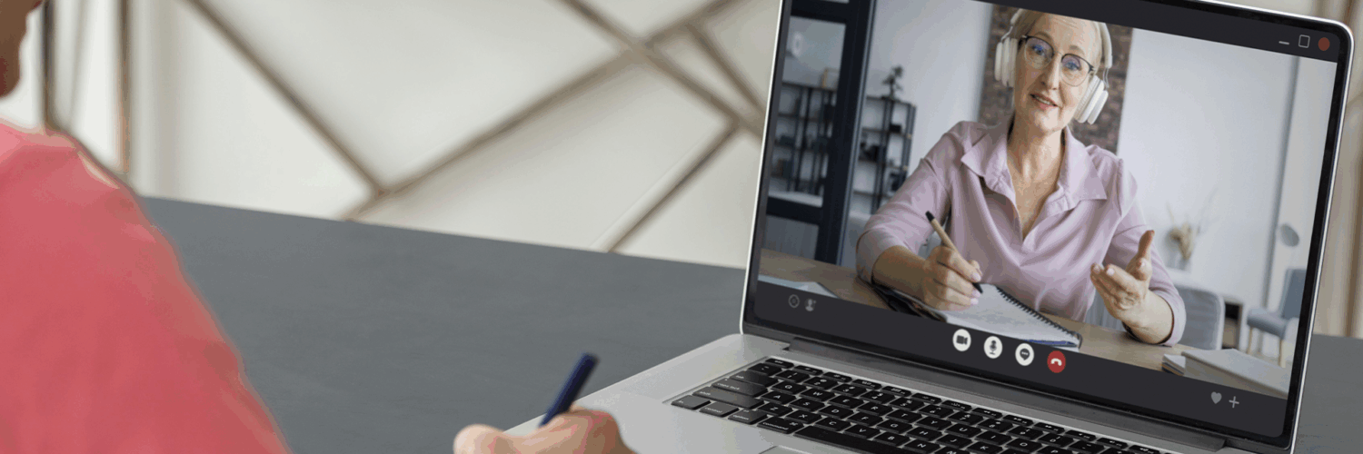 Pessoa participa de aula online pelo notebook, enquanto faz anotações em um caderno durante a videochamada.