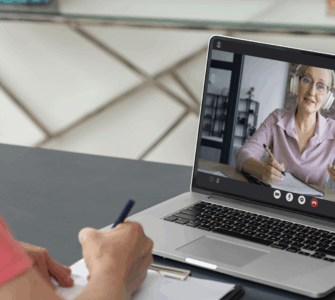 Pessoa participa de aula online pelo notebook, enquanto faz anotações em um caderno durante a videochamada.