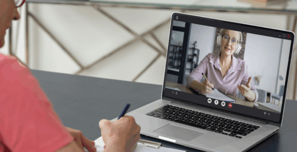 Pessoa participa de aula online pelo notebook, enquanto faz anotações em um caderno durante a videochamada.