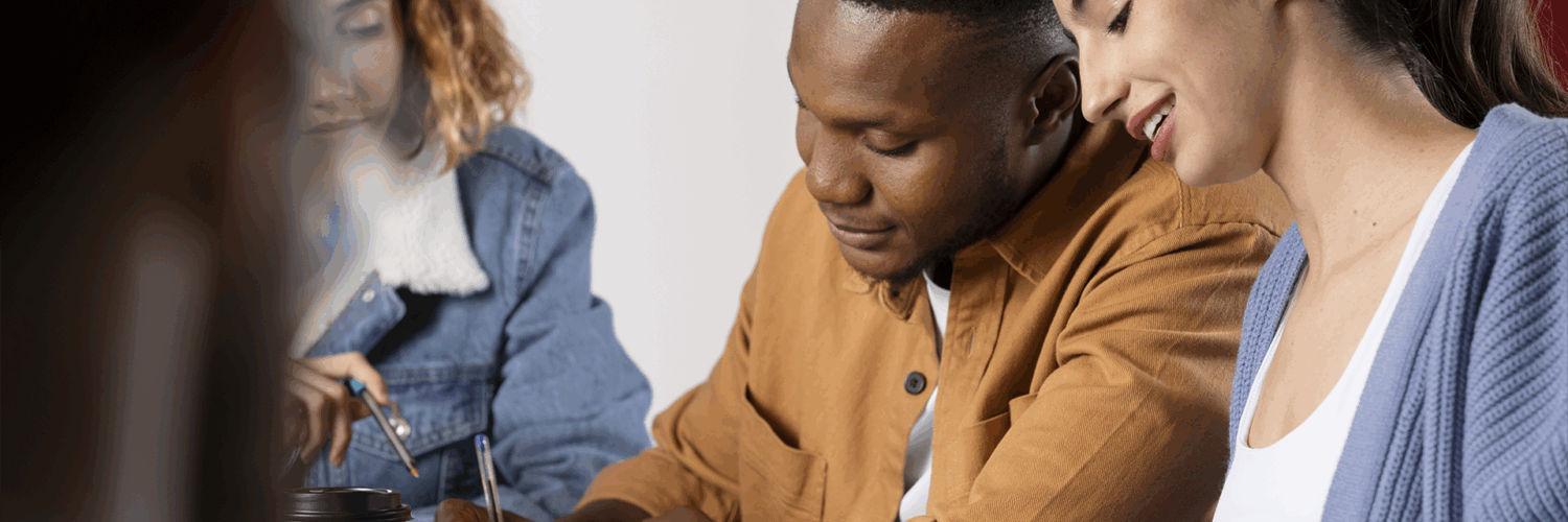 Grupo de jovens estudando juntos em mesa, trocando ideias e escrevendo em cadernos com atenção e colaboração.