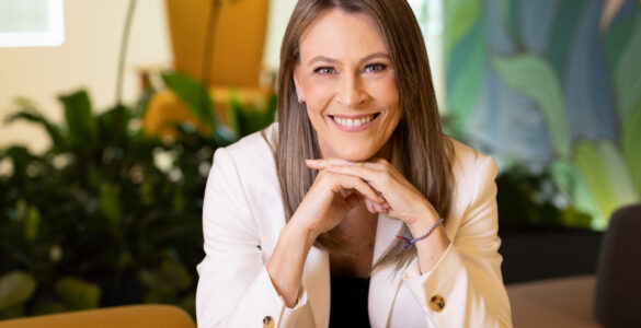 Ana Claudia Plihal sorridente de blazer branco em ambiente corporativo, transmitindo profissionalismo e confiança.