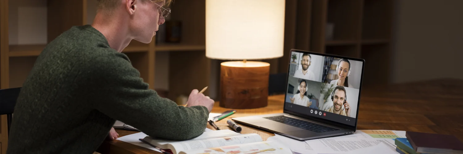 Estudante em videoconferência no notebook, estudando com livros e anotações sobre ensino a distância.