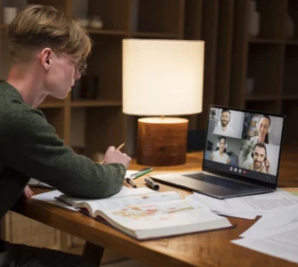 Estudante em videoconferência no notebook, estudando com livros e anotações sobre ensino a distância.
