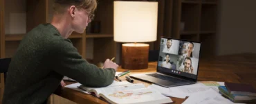 Estudante em videoconferência no notebook, estudando com livros e anotações sobre ensino a distância.