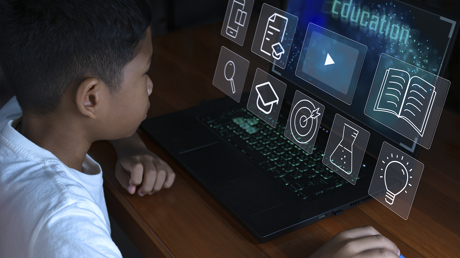 Um menino observa uma tela de laptop com ícones educativos digitais e as palavras "educação" e "e-learning".