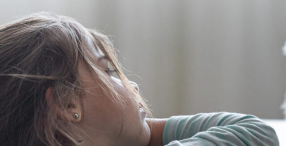 Menina observa pensativa seu ursinho de pelúcia sobre a mesa, em ambiente suave e iluminado.