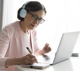 Mulher madura em casa, de fone de ouvido, estudando online. Ilustra as mudanças no EAD e o aprendizado remoto.