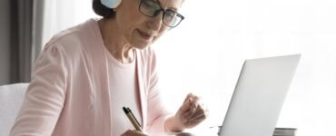 Mulher madura em casa, de fone de ouvido, estudando online. Ilustra as mudanças no EAD e o aprendizado remoto.