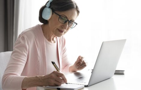 Mulher madura em casa, de fone de ouvido, estudando online. Ilustra as mudanças no EAD e o aprendizado remoto.