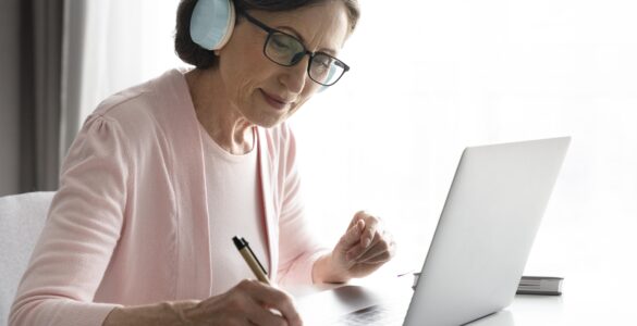 Mulher madura em casa, de fone de ouvido, estudando online. Ilustra as mudanças no EAD e o aprendizado remoto.