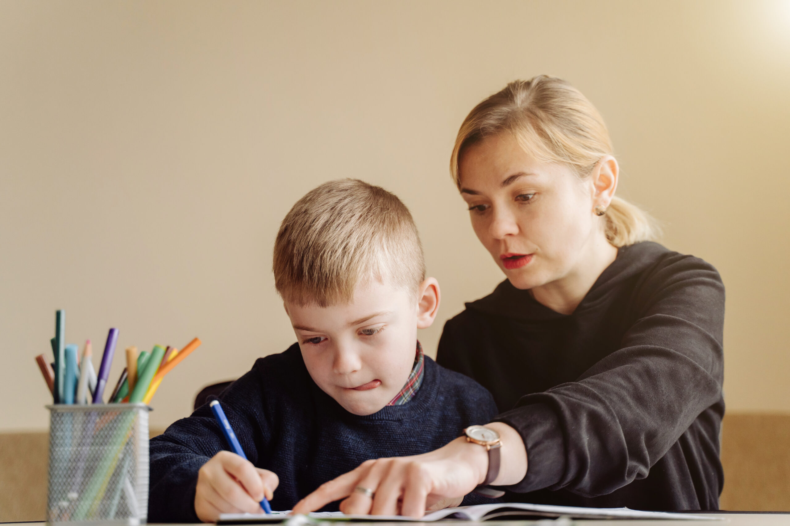 Mother using laptop and tablet teaching with her son online at home in his room