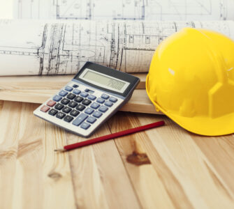 Yellow helmet with blueprints and calculator on wood
