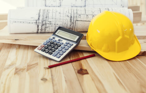 Yellow helmet with blueprints and calculator on wood