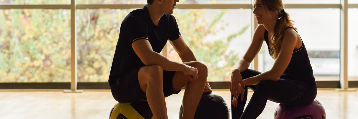 Man and Woman sitting with fitballs in the gym.